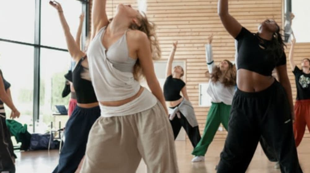 Clase grupal de baile en un salón de madera, con los brazos arriba